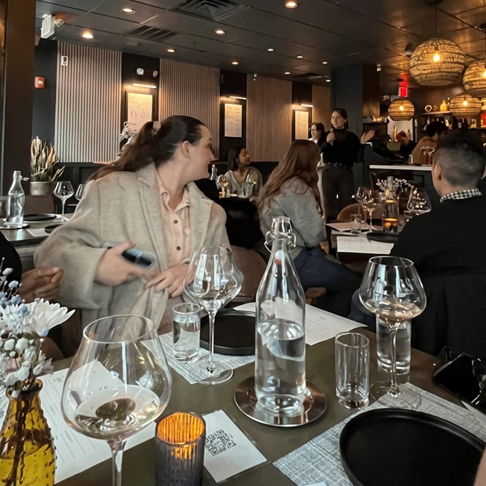Diners enjoy an upscale restaurant with elegant table settings, wine glasses, floral centerpiece, and warm woven pendant lighting.